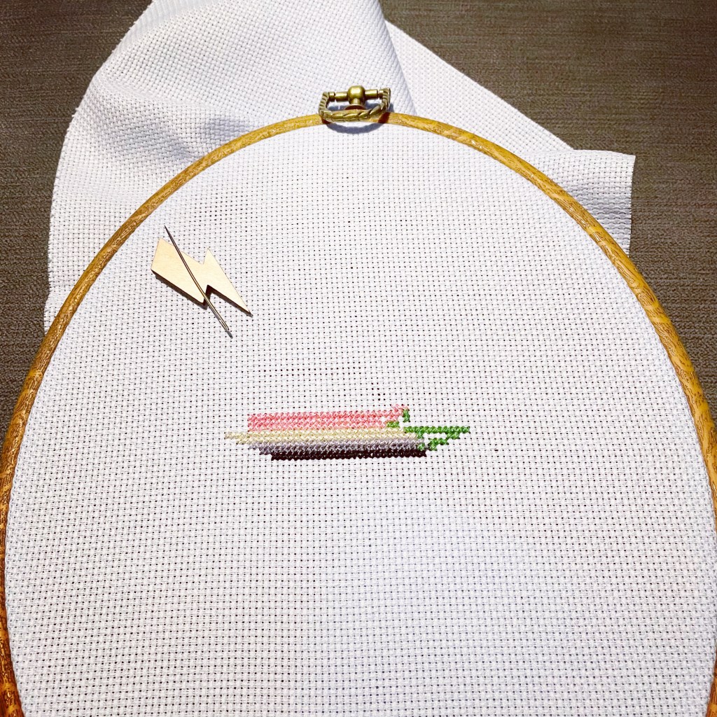 a blue cross stitch cloth, with a half completed pink soap bar.